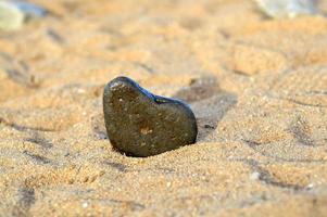 pierre en forme de coeur sur fond de plage. journée d'été ensoleillée. concept d'amour, de mariage et de saint valentin. trouver des pierres belles et intéressantes. vacances à la plage photo