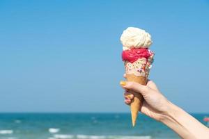 main tenant un cornet de crème glacée avec fond de ciel bleu photo