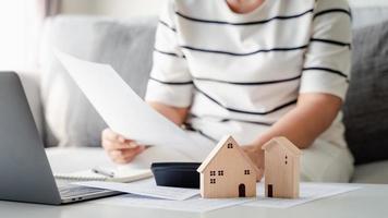 femme calcule l'hypothèque de prêt immobilier pour récapituler les paiements de dépenses à l'aide d'une calculatrice et d'un ordinateur portable, avec un petit modèle de maison en bois, prévoit d'acheter une propriété, des concepts de prêt immobilier. photo