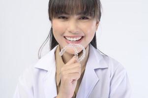 jeune femme dentiste tenant des accolades invisalign sur fond blanc studio, soins dentaires et concept orthodontique. photo