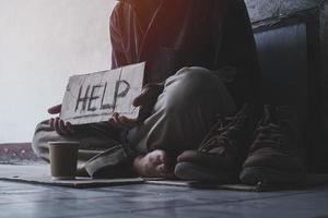 homme adulte sans-abri assis dans la rue à l'ombre du bâtiment et mendiant de l'aide et de l'argent avec un signe. notion de sans-abri. photo