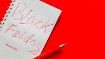 texte de vente du vendredi noir écrit sur un bloc-notes avec un crayon rouge sur fond rouge. arrière-plan, concept de vacances. vendredi noir - journée internationale du shopping, des promotions, des remises, des soldes. photo