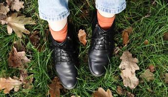 jambes féminines en bottes noires sur l'herbe verte avec des feuilles d'automne jaunes tombées dans le parc. notion d'automne. chaussures pour femmes en feuillage d'automne photo