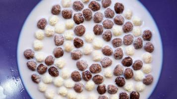 petit déjeuner sain avec du lait sur la table dans une assiette profonde. boules de chocolat et de lait de grains entiers. petit-déjeuner sain aux céréales. petit-déjeuner des enfants. nourriture pour bébés. régime équilibré. collation sèche et rapide photo