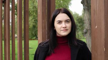 portrait d'une belle femme caucasienne portant un manteau noir et un pull rouge tout en marchant à l'extérieur dans un parc de la ville avec un arrière-plan flou. une femme regarde la caméra par une journée ensoleillée. photo