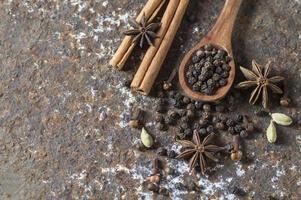 épices et herbes. ingrédients de la nourriture et de la cuisine. bâtons de cannelle, étoiles d'anis, grains de poivre noir et cardamome sur fond texturé. photo