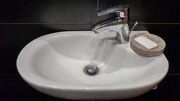 intérieur de la salle de bain avec lavabo et robinet. appartement moderne dans les combles de la maison. lavabo en céramique blanche avec robinet chromé sur un mur de carreaux noirs photo