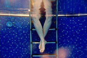 les jambes des hommes dans les escaliers sous l'eau dans la piscine en été photo