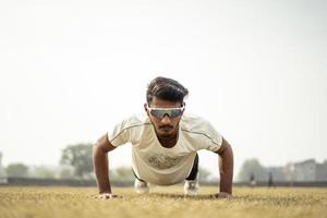 portrait en gros plan d'un jeune sportif indien exerçant sur le terrain. sportif faisant des pompes pour s'échauffer. photo