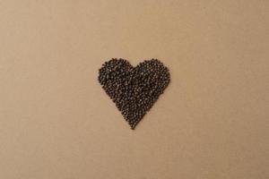 coeur fait de grains de poivre noir sur fond de papier kraft respectueux de l'environnement. carte de saint valentin créative photo