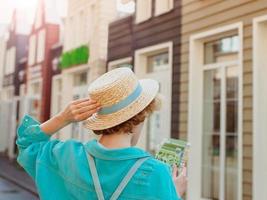 dos de jeune femme rousse au chapeau de paille et avec sac de voyage avec carte papier voyage en europe de l'ouest. photo de voyage et lifestyle