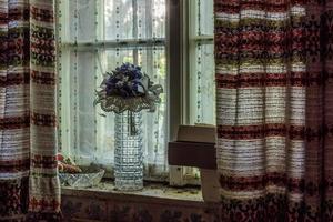 vase de verre avec des fleurs sur un rebord de fenêtre avec de vieux rideaux photo