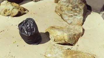 sac poubelle en plastique noir plein de déchets sur la plage photo