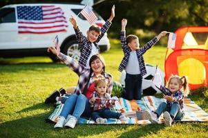 famille américaine passer du temps ensemble. avec des drapeaux américains contre une grosse voiture suv en plein air. photo