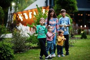 quatre enfants avec leur mère mangent des beignets dans la cour du soir. délicieux beignets délicieux. photo