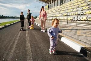 jeune mère élégante avec quatre enfants en plein air. la famille sportive passe du temps libre à l'extérieur avec des scooters et des patins. photo