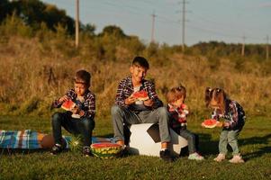 la famille passe du temps ensemble. quatre enfants mangent de la pastèque en plein air. photo