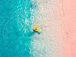 vue aérienne de drone d'une fille flottant sur un ananas gonflable sur une plage rose tropicale exotique photo