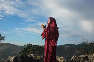 jeune femme musulmane avec hijab ou écharpe priant dans la nature en plein air sur un ciel bleu vif, mains en prière, prière méditative musulmane, prière musulmane photo