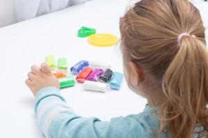 la fille à table joue avec de la pâte à modeler. jeux pour enfants pour la motricité fine photo