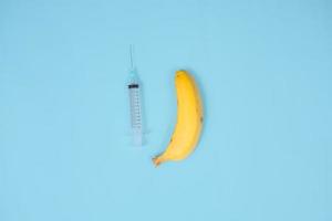 seringue, banane et contraception isolées sur fond bleu photo