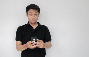 wow le visage de votre homme asiatique a choqué ce qu'il voit dans le smartphone sur fond gris isolé. indonésie homme porter chemise noire isolé fond gris photo