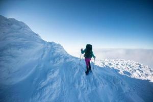 une femme avec un sac à dos en raquettes grimpe une montagne enneigée photo