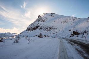 soleil sur la montagne enneigée avec route rurale en hiver sur les îles lofoten photo