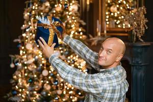 un homme avec un cadeau près du sapin de noël photo