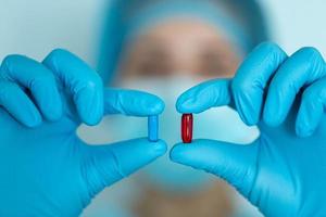 les mains du médecin dans un gant en latex bleu tiennent des capsules médicales rouges et bleues