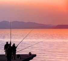 silhouette de pêcheurs pêchant au coucher du soleil sur la mer photo