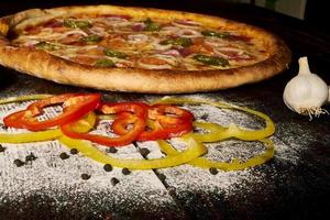 pizza au pepperoni avec jambon et piments jalapeno sur une vieille table en bois photo