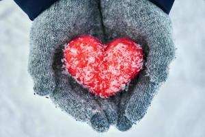 mains féminines dans des gants de laine tenant un coeur de laine rouge avec des flocons de neige à l'extérieur photo