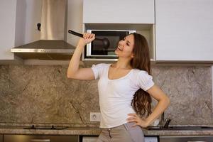 une jeune femme chante dans une cuisine moderne avec une louche photo