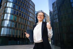 une femme d'affaires se tient avec un ordinateur portable près d'un immeuble de bureaux photo