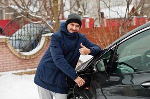 jeune homme chargeant sa voiture électrique en hiver. concept de transport écologique. photo