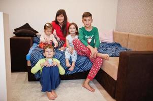 une grande famille heureuse s'amuse ensemble dans la chambre. grand concept de matinée familiale. mère de quatre enfants porte un pyjama au lit à la maison. photo