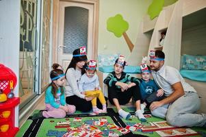 famille heureuse avec quatre enfants jouant au jeu devinez qui tout en s'amusant à la maison. photo