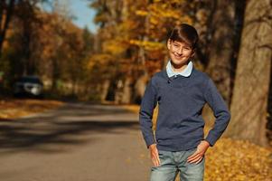 un jeune garçon adolescent porte un polo, un pull bleu et un jean pose sur fond d'automne. photo