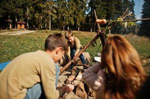 feu de joie familial en montagne. faire frire des saucisses. mère avec quatre enfants en camping. randonnée d'automne et météo du camp. réchauffer et cuire près de la flamme ensemble. photo