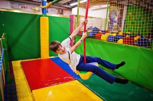 garçon souriant se balançant sur une corde à l'aire de jeux intérieure. photo