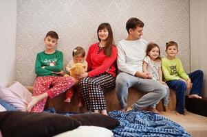 une grande famille heureuse s'amuse ensemble dans la chambre. grand concept de matinée familiale. quatre enfants avec des parents portent un pyjama au lit à la maison. photo