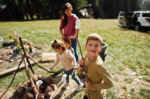 feu de joie familial en montagne.quatre enfants en camping. guimauve barbecue. randonnée d'automne et météo du camp. réchauffer et cuire près de la flamme ensemble. photo