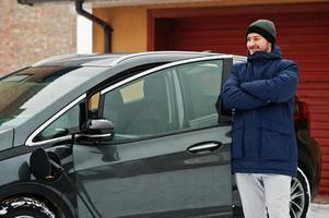 jeune homme chargeant sa voiture électrique en hiver. concept de transport écologique. photo