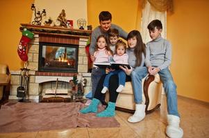 heureuse jeune famille nombreuse à la maison près d'une cheminée dans un salon chaleureux le jour de l'hiver. photo