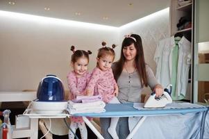 femme mère et ses deux filles enfant filles comme petite aide repassant à la maison. photo