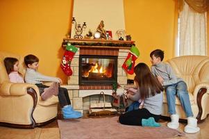 heureuse jeune famille nombreuse près d'une cheminée dans un salon chaleureux le jour de l'hiver. mère avec quatre enfants à la maison. photo