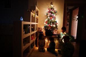 enfants regardant sur l'arbre de noël avec des guirlandes brillantes le soir à la maison. photo