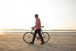 cycliste marchant avec un vélo noir rétro au lever du soleil dans le désert photo