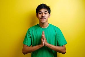 jeune homme asiatique en t-shirt vert souriant et montre un geste de salutation asiatique photo